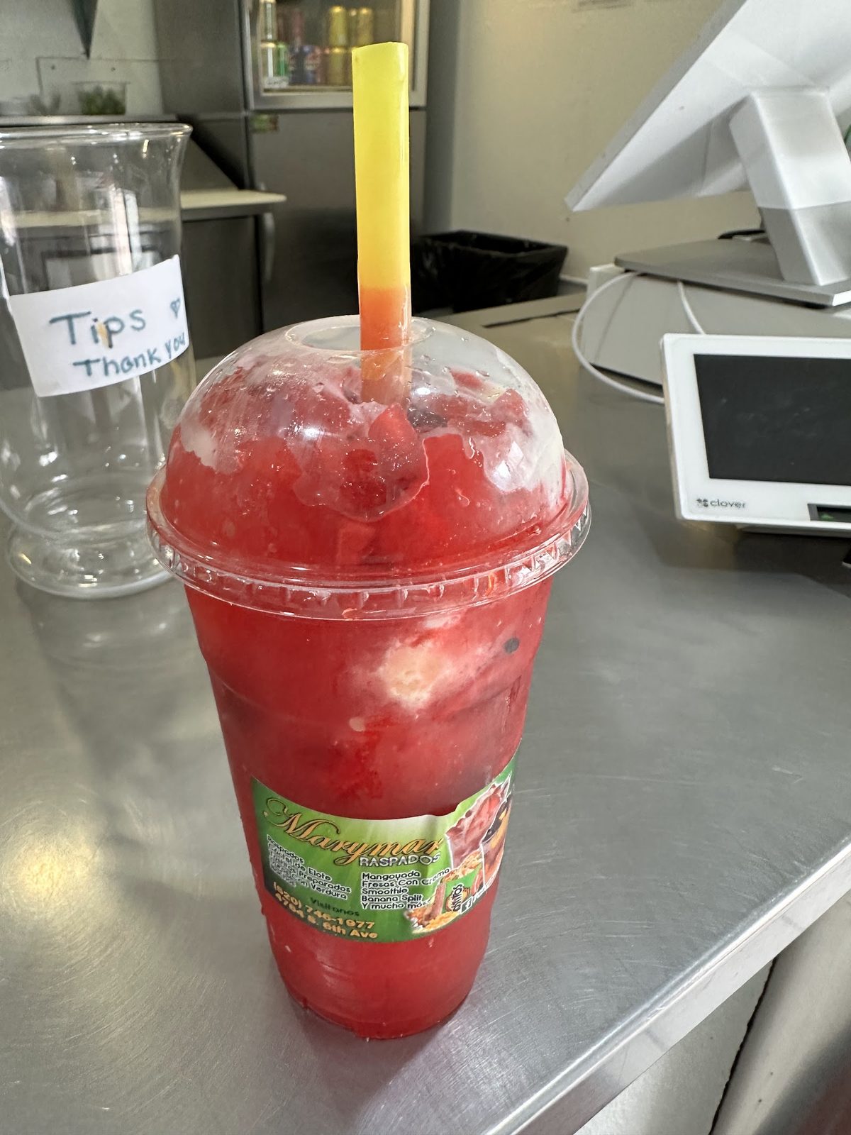 A tall cup of strawberry raspado with a straw, made fresh at the counter.