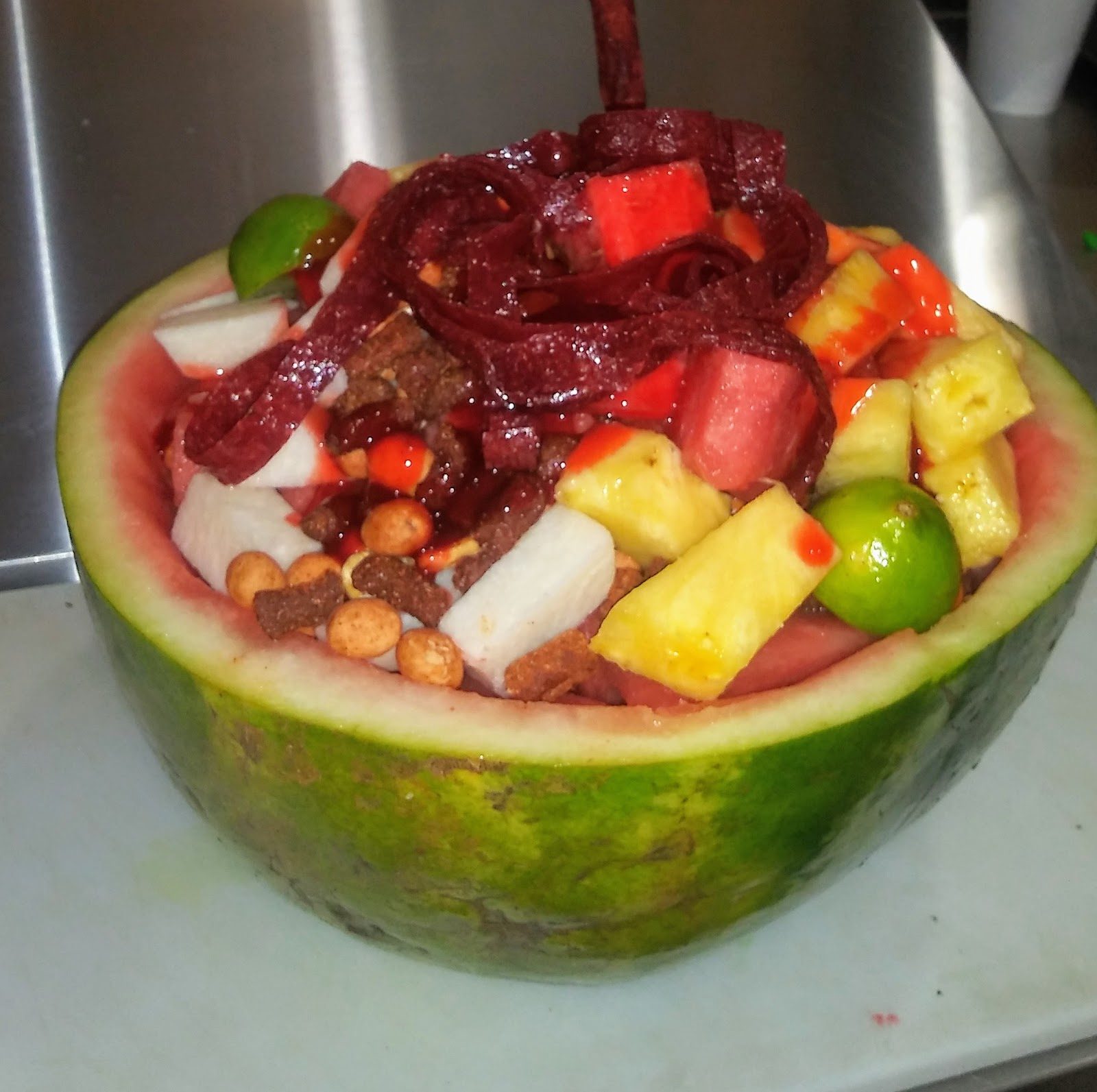 A whole watermelon half filled with chopped fruit, chamoy and candy.
